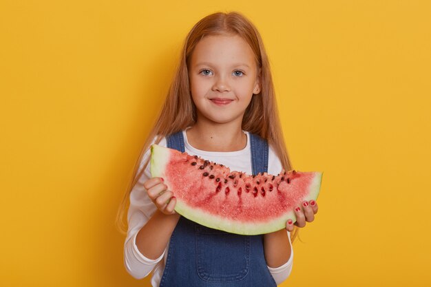 Indoor shot of little charming girl with portion of sweet watermelon in her hands