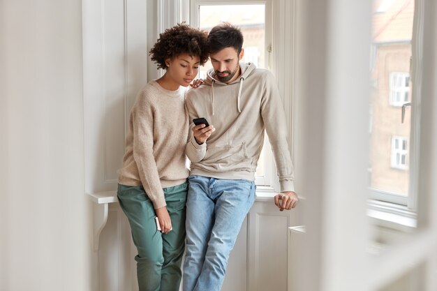 Indoor shot of mixed race girlfriend and boyfriend watch video online via cell phone