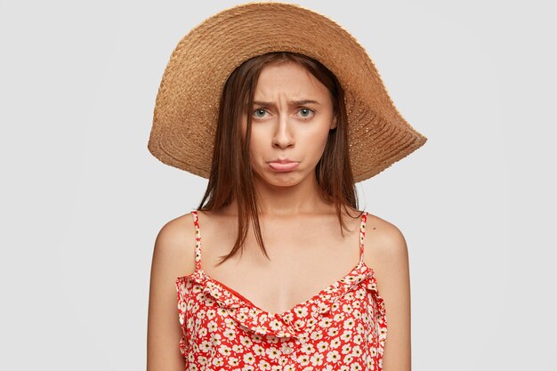 Indoor shot of offended sad woman in summer hat and red dress