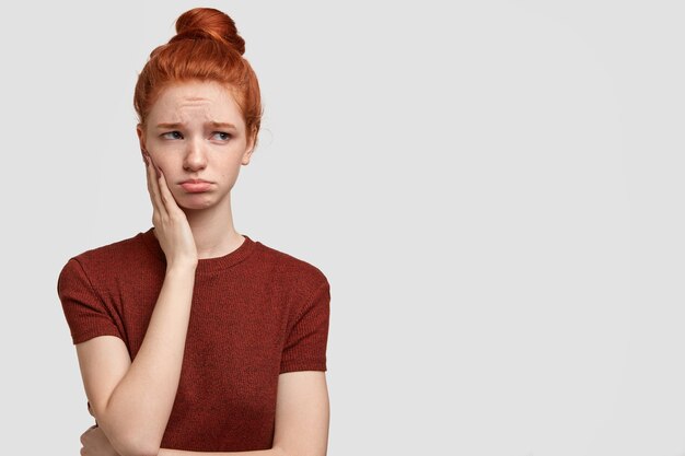 Indoor shot of offended teenager purses lips, looks with dejected expression aside