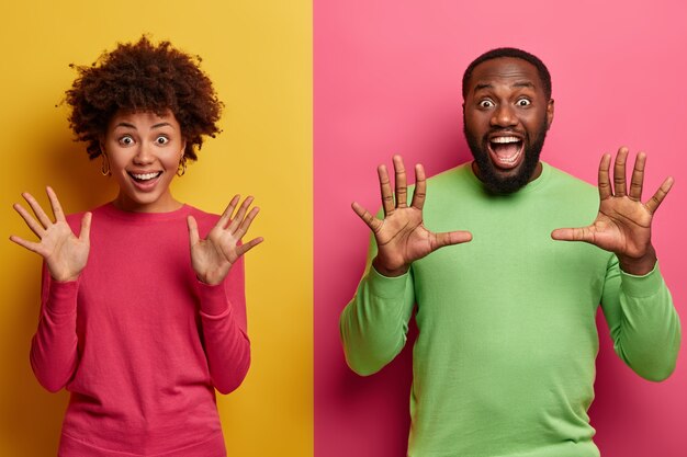 indoor shot of overjoyed overemotive ethnic woman and man raise palms, stare emotionally, glad to see amazing surprise, open mouthes