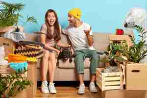 Free photo indoor shot of overjoyed young couple sitting on the couch surrounded by boxes