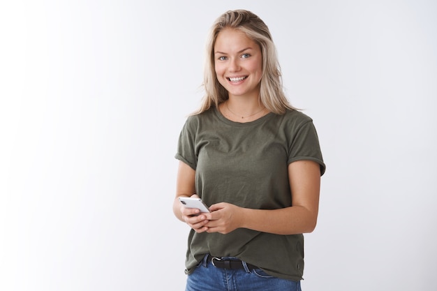 Free photo indoor shot of pleasant good-looking positive woman receiving heartwarming video in app smiling delighted at camera holding smartphone checking messages posting pic in social network