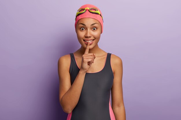 Indoor shot of pleasant looking professional swim coach tells secret of successful swimming, makes silence gesture