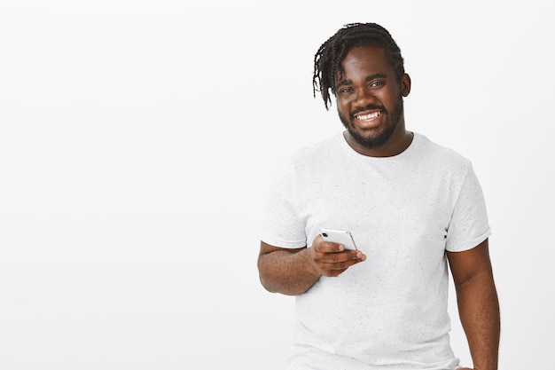 Indoor shot of positive guy with braids posing against the white wall