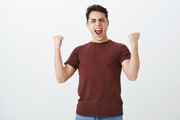 Indoor shot of positive triumphing handsome football fan in casual red t-shirt