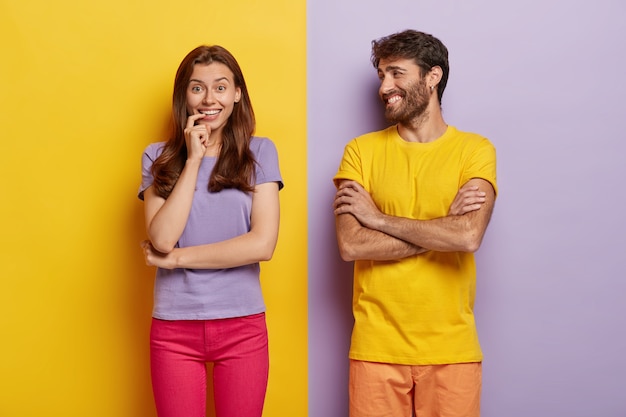 Free photo indoor shot of positive young woman and man smile happily, being in good mood, spend free time together, wear t shirts