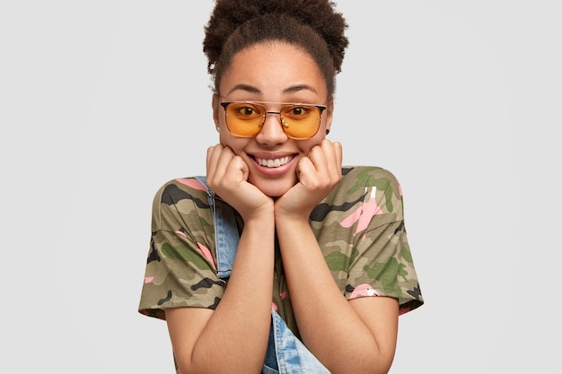 Indoor shot of pretty dark skinned woman keeps both hands under chin