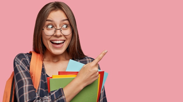 Indoor shot of pretty student posing against the pink wall with glasses