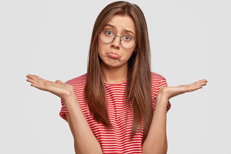 Free Photo indoor shot of pretty young displeased woman shruggs shoulders with hesitation, looks doubtfully at camera