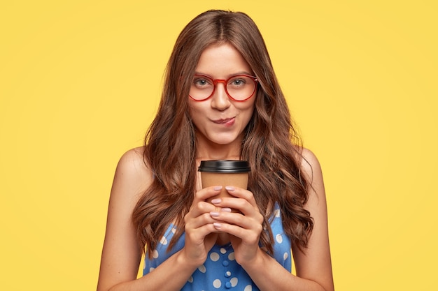 Indoor shot of pretty young woman with glasses posing against the yellow wall
