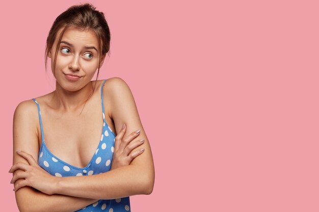 Indoor shot of puzzled hesitant woman keeps hands crossed