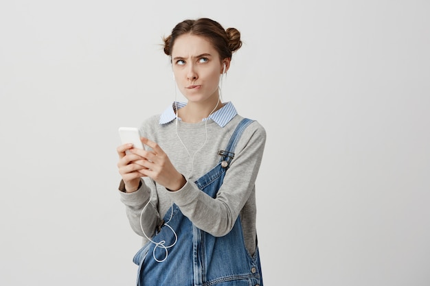 Free photo indoor shot of resentful adult girl posing with her cellphone in hands biting her lips in irritation. female person being offended with received text while social networking. human reactions