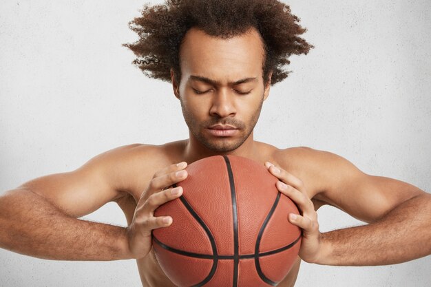 Indoor shot of serious concentrated basketball player with ball prepares alone for important match