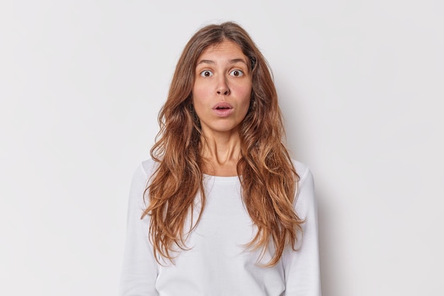 Free photo indoor shot of shocked amazed young woman with long hair stares with surprisement holds breath keeps mouth opened wears casual jumper isolated over white background human reactions concept