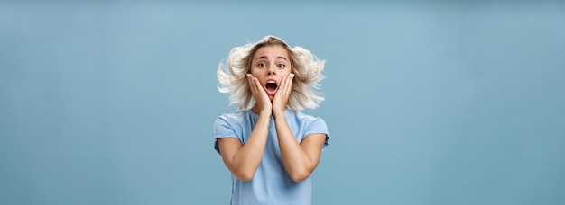 Free photo indoor shot of shocked and impressed young stylish european female with blond hair holding hands on