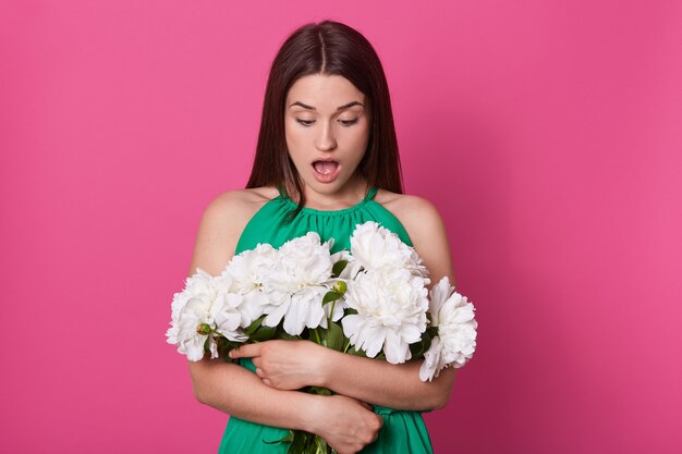 Indoor shot of shocked impressed young woman looking at bouquet with open mouth