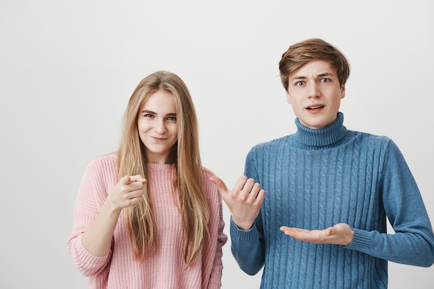 Indoor shot of shocked male and frowning female wearing colourful sweaters