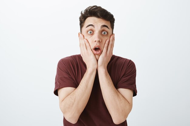 Indoor shot of shocked and stunned handsome man in red t-shirt, dropping jaw