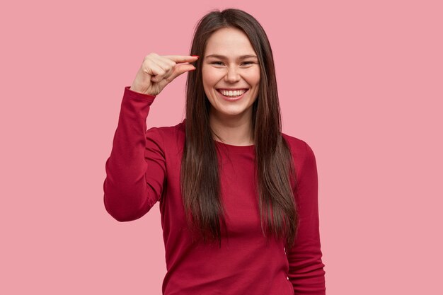 Indoor shot of smiling woman shows little amount of something, gestures with hand, being in high spirit