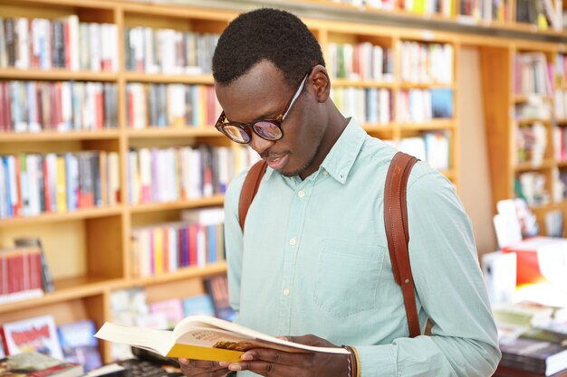 Indoor shot of student in glasses looking through book in his hands