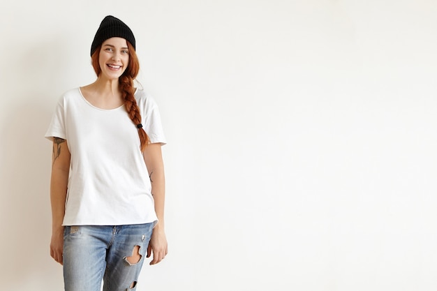 Indoor shot of stylish Caucasian young redhead woman wearing trendy black hat