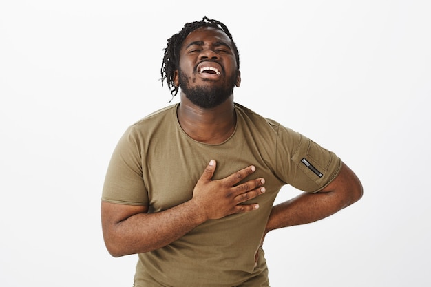 Indoor shot of a suffering guy in a brown t-shirt posing against the white wall