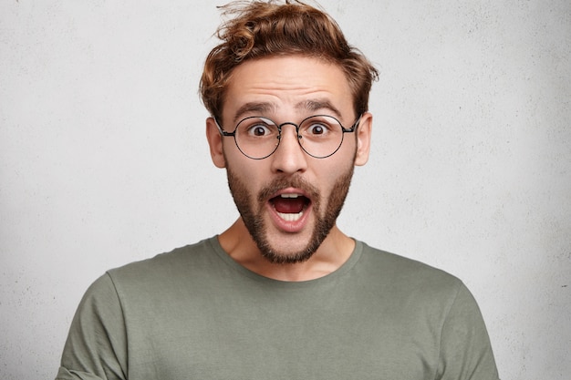 Free photo indoor shot of surprised european man opens mouth widely, being shocked