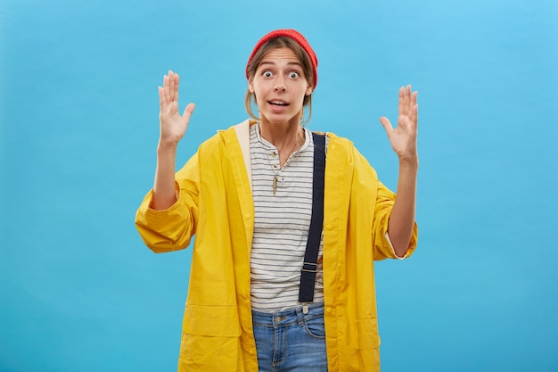 Indoor shot of surprised female worker showing size. Beautiful female demonstrating size of something big or huge with hands. Astonished female gesturing over blue wall