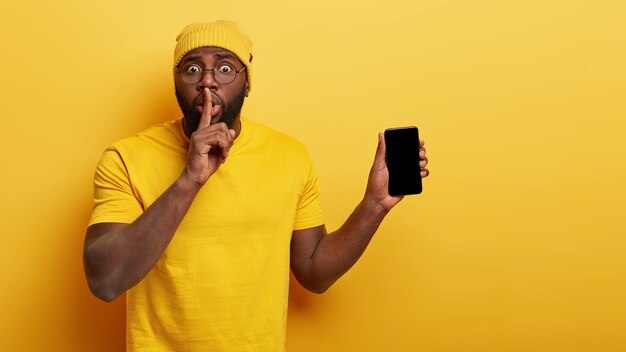 Indoor shot of surprised handsome guy with glasses posing with his phone