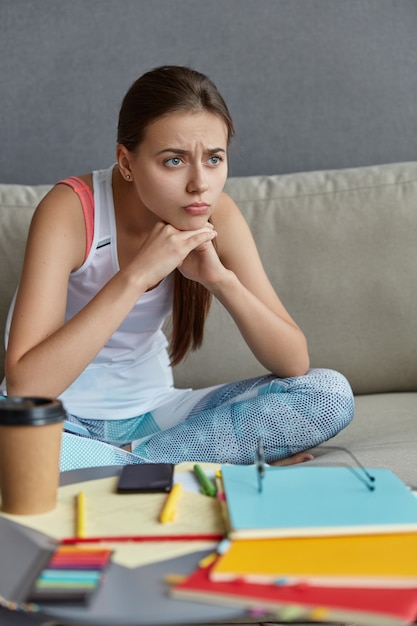 Indoor shot of thoughtful European freelancer focused into distant, thinks about something