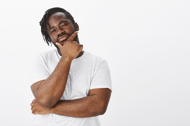 Indoor shot of thoughtful guy with braids posing against the white wall