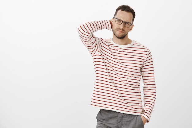Indoor shot of troubled tired businessman in striped clothes, scratching back of neck