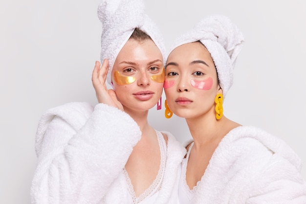 Indoor shot of two diverse women stand closely to each other apply collagen patches under eyes Free Photo