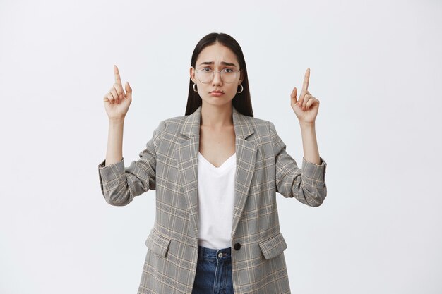 Tシャツの上に眼鏡とジャケットを着て、悲しみから顔をしかめ、上向きに、動揺して不快な魅力的な女性の屋内ショット