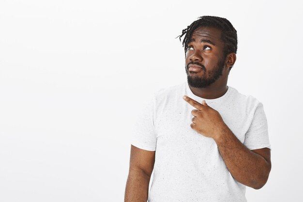 Indoor shot of worried guy with braids posing against the white wall