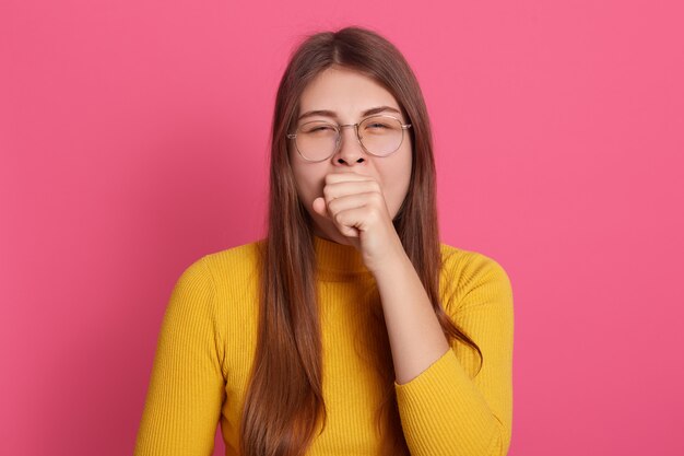 Indoor shot of yawning girl wearing glasses and casual yellow shirt