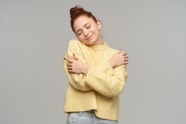 Free photo indoor studio portrait of young ginger female with freckles posing over grey background hug herself