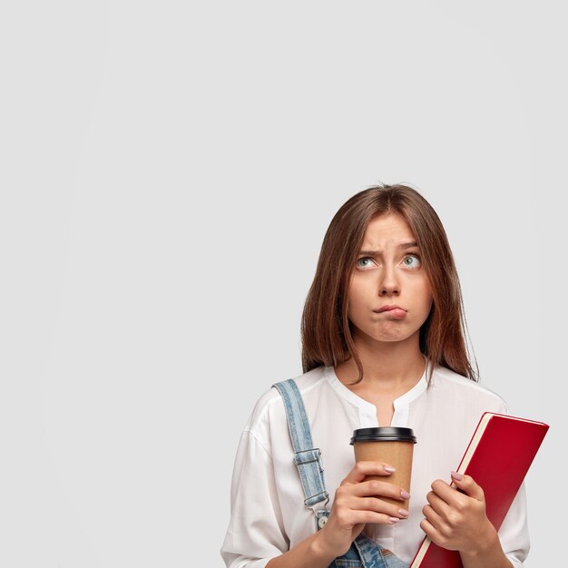 Indoor vertical shot of pleasant stylish teenager posing against the white wall