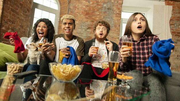 Indoors. Excited people watching sport match, championship at home. Multiethnic group of friend, fans cheering for favourite sport team