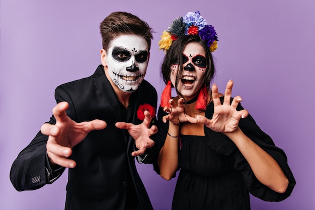 Indoors snapshot of man in suit and woman with crown of flowers posing with frightening facial expressions.