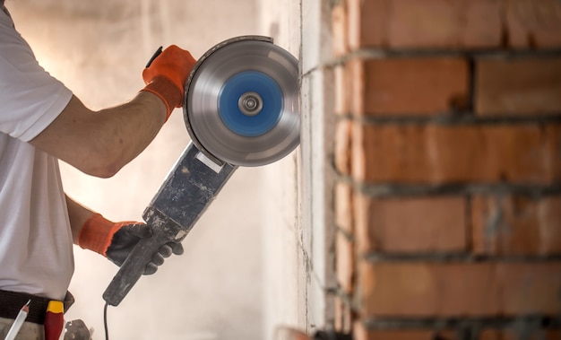 The industrial Builder works with a professional angle grinder to cut bricks and build interior walls. Electrician.