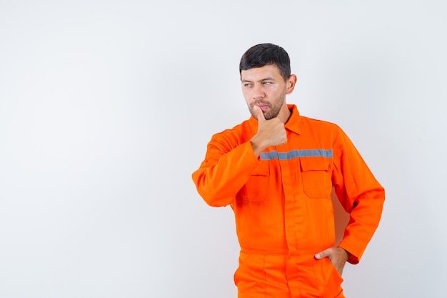 Industrial man looking away with finger in lips in uniform and looking pensive. front view.