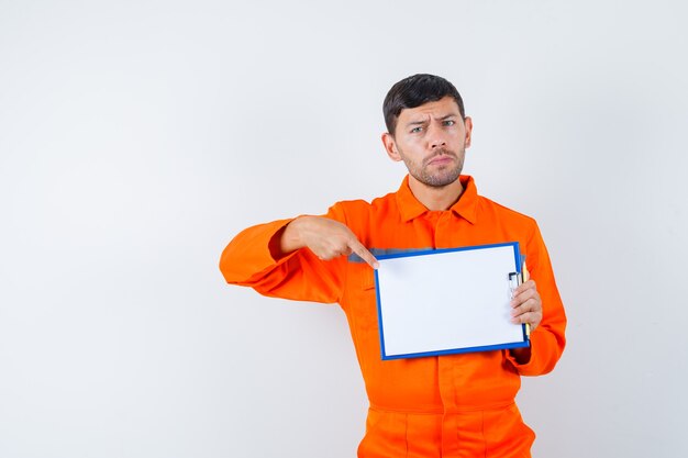 Industrial man pointing at clipboard in uniform and looking serious , front view.