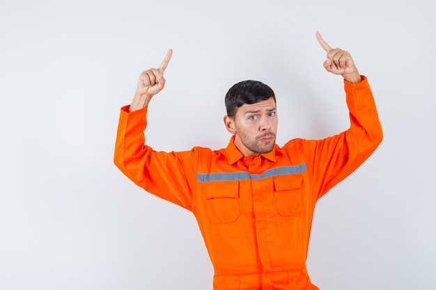 Industrial man pointing up in uniform and looking confident. front view.