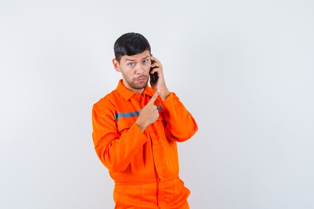 Industrial man talking on mobile phone, pointing at right corner in uniform front view.