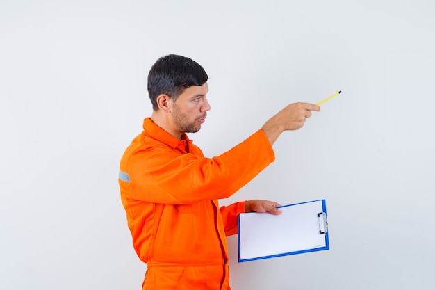 Industrial man in uniform giving instructions, holding pencil, clipboard.