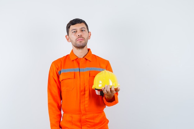 Industrial man in uniform holding helmet and looking calm , front view.