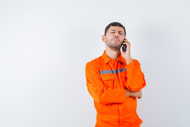 Промышленный человек в униформе разговаривает по мобильному телефону и смотрит задумчиво, вид спереди.
