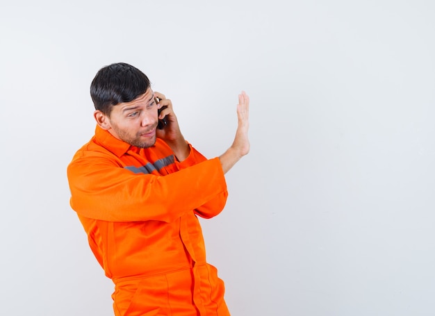 Industrial man in uniform talking on mobile phone with stop gesture , front view.